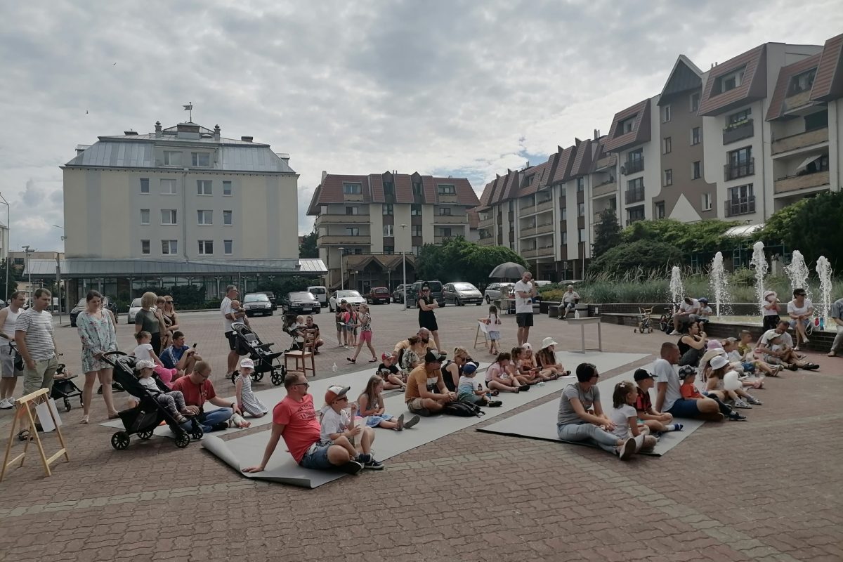 Publiczność siedząca na placu przy fontannie