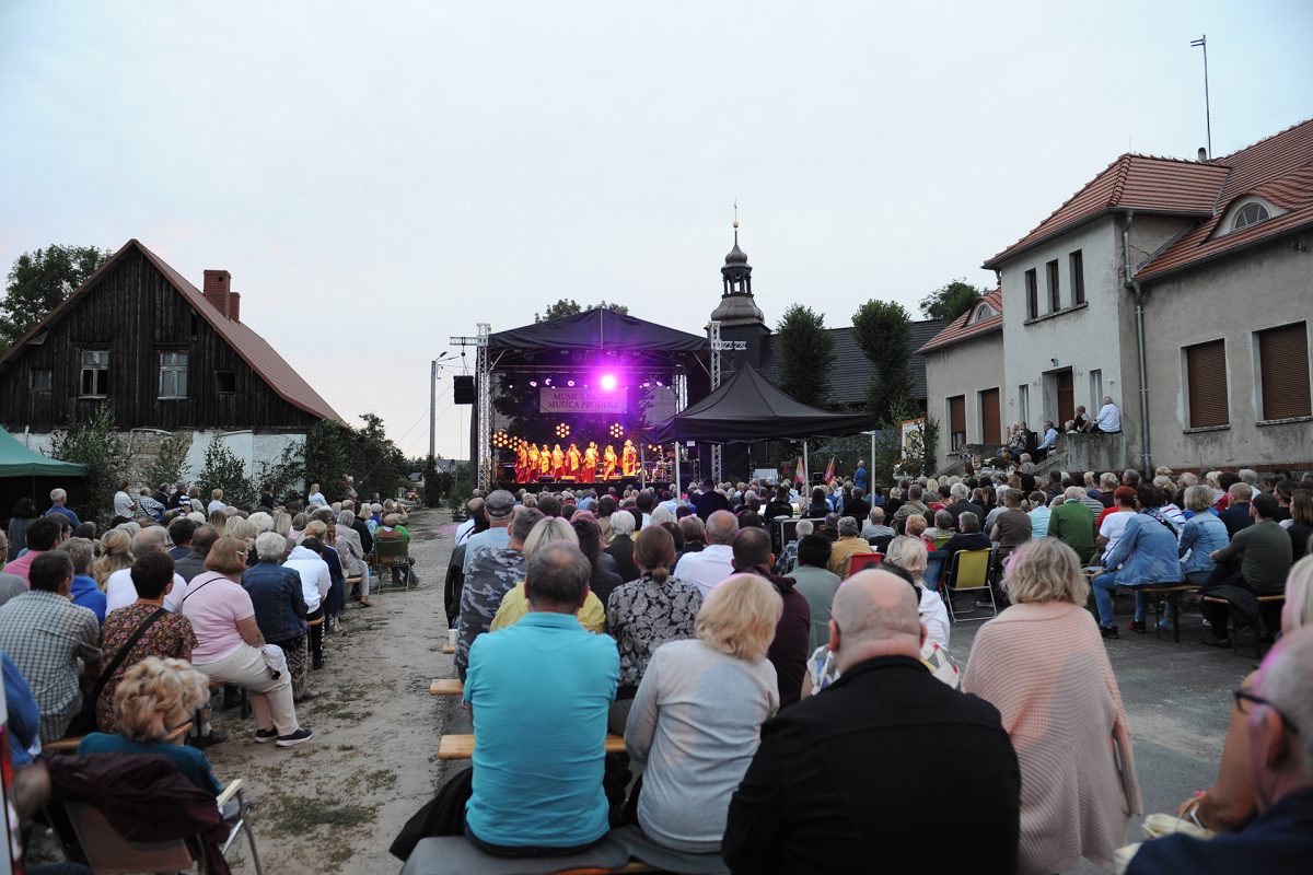 Publiczność festiwalowa siedzi na ławkach w tle scena