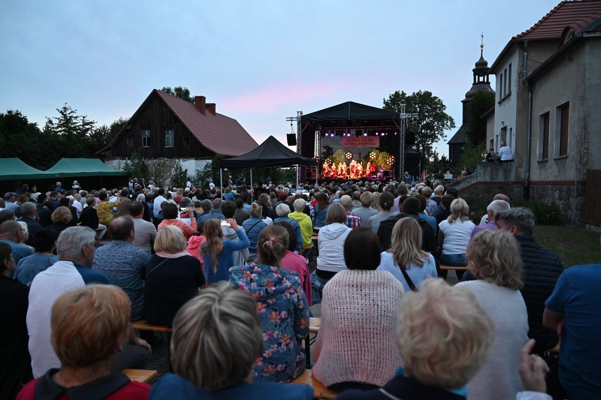 Publiczność festiwalowa siedzi na ławkach w tle scena