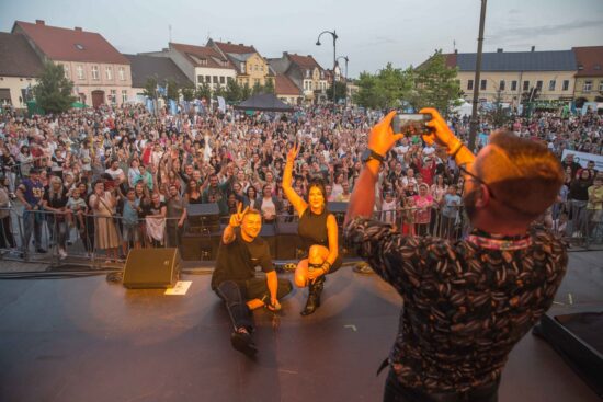 Artyści na scenie, tłum publiczności przed sceną.