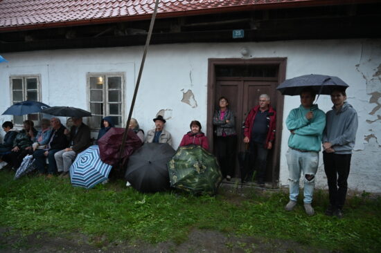 Publiczność pod ścianą budynku z parasolami