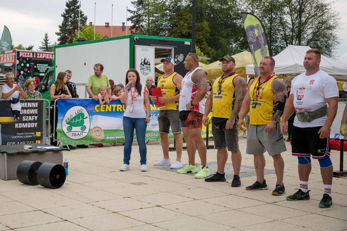 Pani burmistrz mówi przez mikrofon obok strongmani.