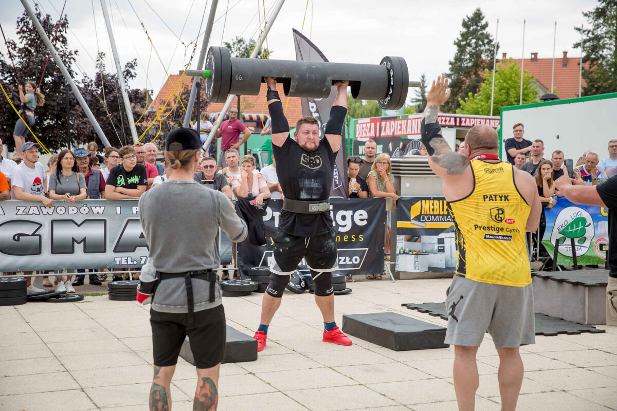 Strongman podnosi ciężar, publiczność w tle.