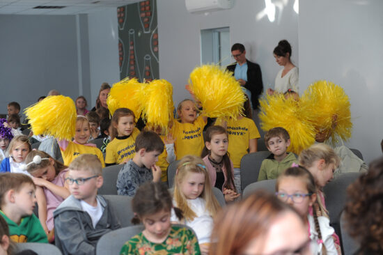 Dzieci w żółtych koszulkach z pomponami dopingują uczestników