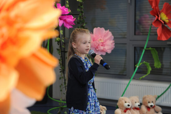 Dziewczynka śpiewa na scenie, w tle motywy kwiatowe