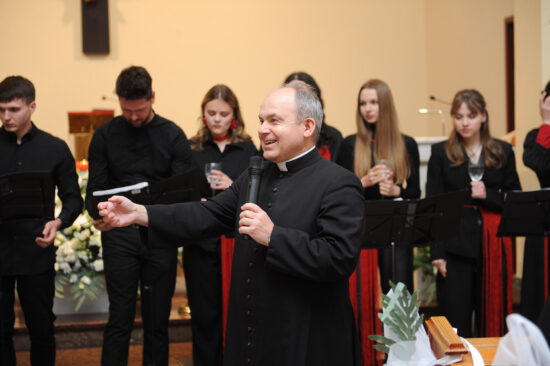 Ksiądz mówi przez mikrofon, chór w tle