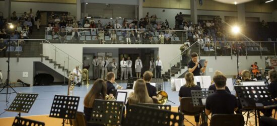 Muzycy orkiestry dętej wraz z kapelmistrzem, w tle publiczność
