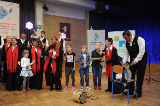 Chór na scenie wraz z grającymi dziećmi na instrumentach perkusyjnych