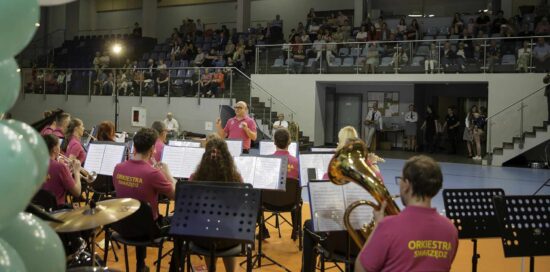 Muzycy orkiestry dętej wraz z kapelmistrzem, w tle publiczność