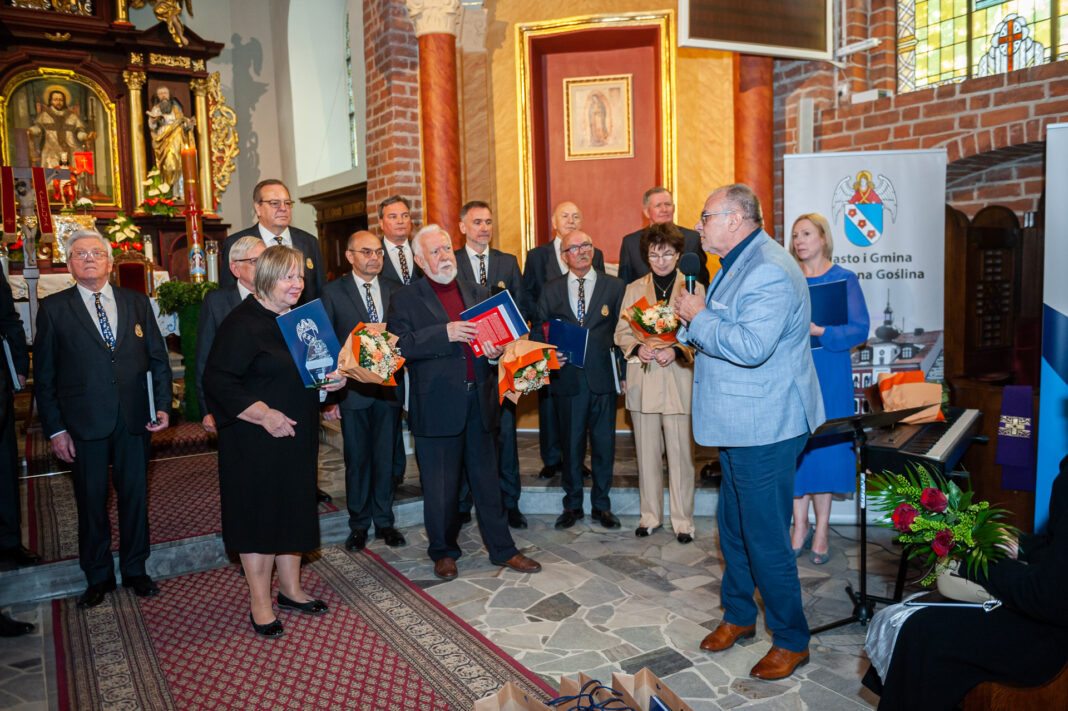 27 mężczyzna z mikrofonem, za nim wszyscy dyrygenci i chór