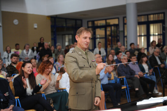 Kapelmistrz dyrygujący orkiestrą w tle publiczność