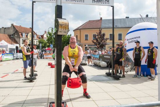 Strongman przerzuca ciężar, publiczność w tle.