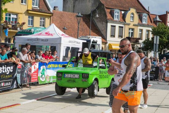 Strongman przenosi aut, publiczność w tle.