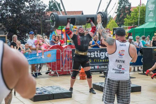 Strongman podnosi ciężar, publiczność w tle.