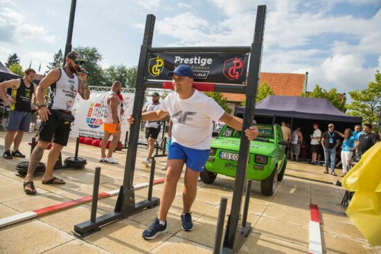 Strongman podnosi ciężar, publiczność w tle.