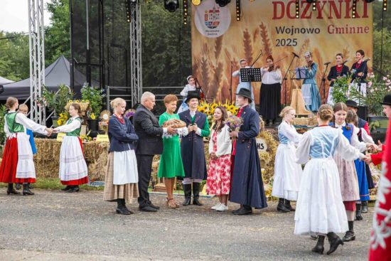 Starostowie dożynek w otoczeniu tancerzy zespołu ludowego wręczają chleb Pani Burmistrz.