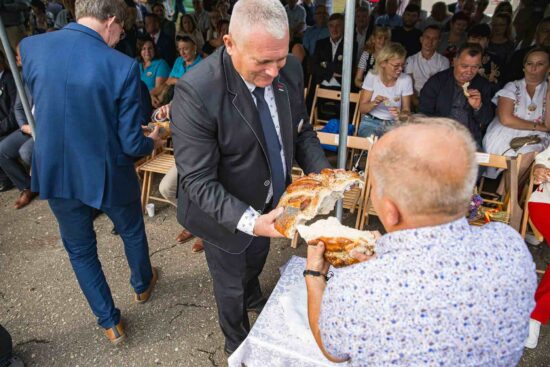 Starosta częstuje ludzi chlebem dożynkowym.
