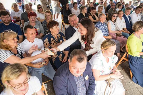 Pani Burmistrz częstuje ludzi chlebem dożynkowym.