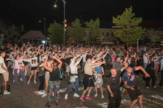 Uczestnicy zabawy jarmarkowej bawiący się przed sceną.