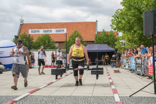 Strongman przenosi ciężar, publiczność w tle.