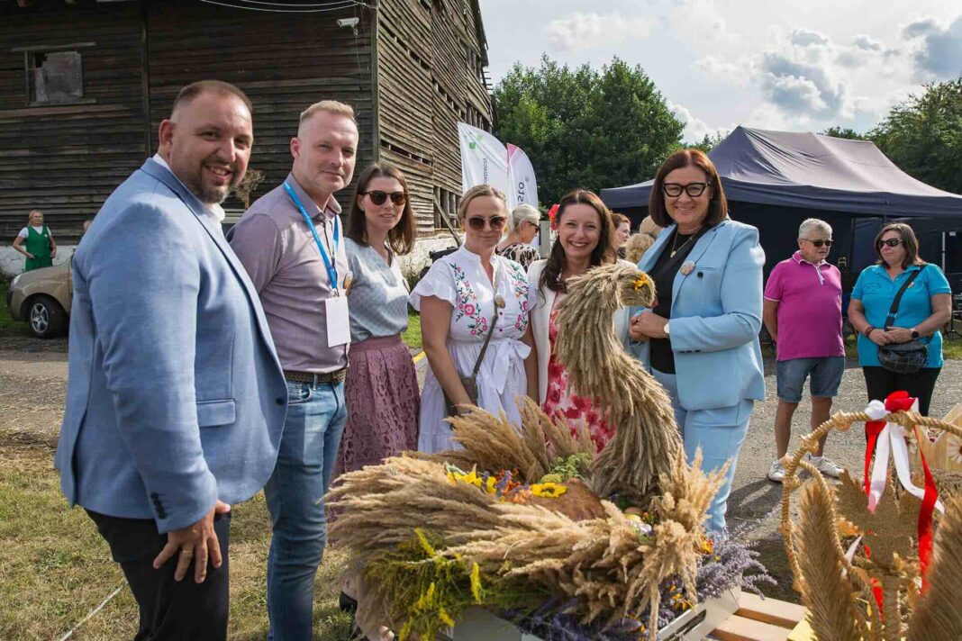 Grupa osób podczas oceny wieńców dożynkowych, przy wieńcu w kształcie łabędzia.