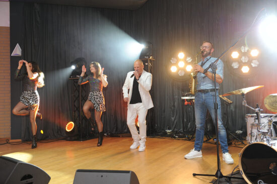 Artysta z mikrofonem, dwie tancerki, muzyk grający na saksofonie oraz DJ na scenie