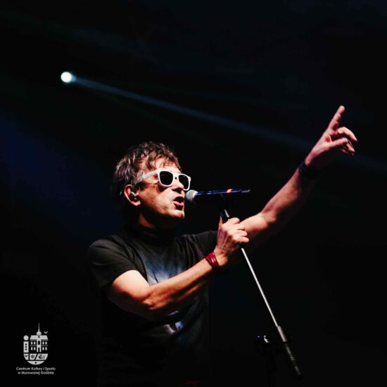 Mężczyzna w okularach na scenie śpiewa do mikrofonu