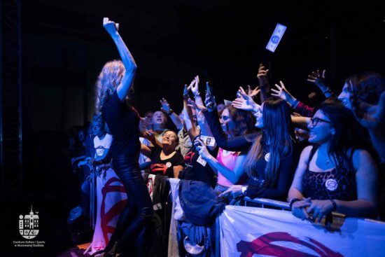 Kobieta rzuca papierkami przypominającymi banknoty wśród publiczności