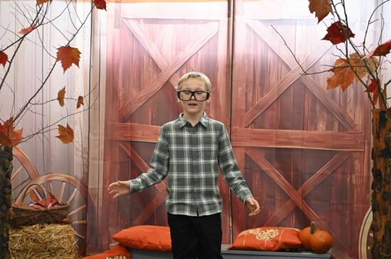 Chłopiec uczestnik konkursu w ogromnych, czarnych okularach na tle jesiennej scenografii