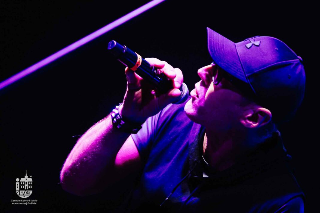 3. Mężczyzna w czapce na scenie śpiewa do mikrofonu