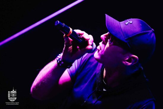 Mężczyzna w czapce na scenie śpiewa do mikrofonu