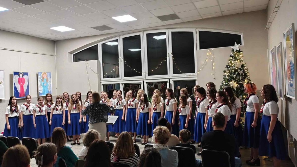 Dziewczęcy Chór Canzona w niebieskich spódnicach stoi przed dyrygentką