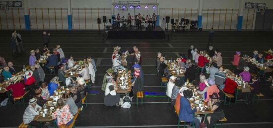 Sala z  seniorami siedzącymi przy stolikach , w tle scena na której występuje Kapela „Swoja Wiara”.