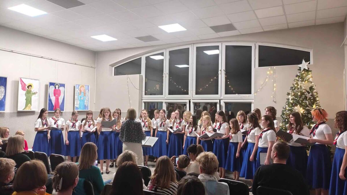 Dziewczęcy Chór Canzona w niebieskich spódnicach stoi przed dyrygentką