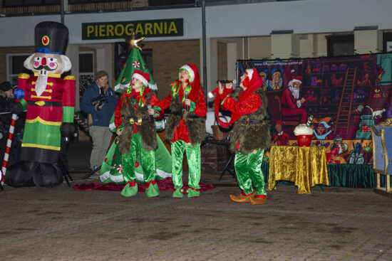 Trójka aktorów przebrana za elfy na tle świątecznej scenografii