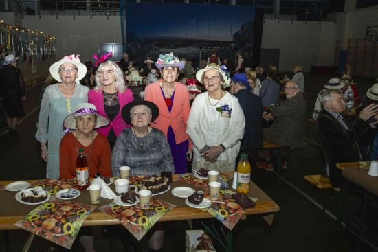 Grupa osób przy stole pozuje do zdjęcia, w tle sala z uczestnikami balu.