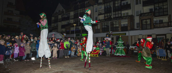 Dwójka szczudlarzy , trójka aktorów przebranych za elfy w tle publiczność i dekoracje świąteczne