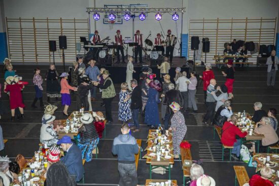 Widok Sali z siedzącymi  i tańczącymi uczestnikami balu w tle scena