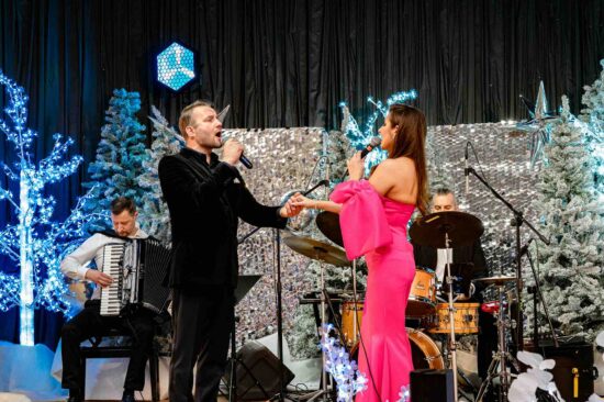 kobieta i mężczyzna śpiewają na scenie, w tle muzycy grający na akordeonie i perkusji