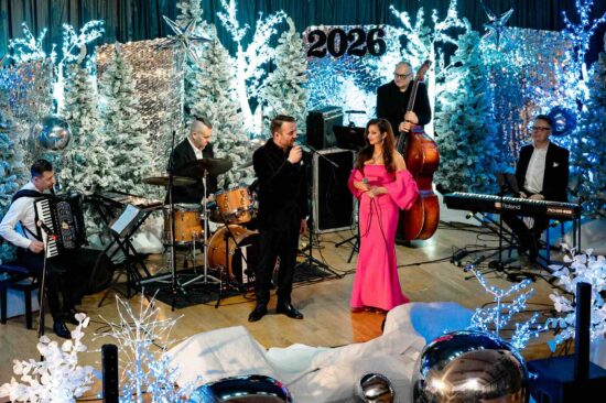 kobieta i mężczyzna śpiewają na scenie, w tle muzycy grający na akordeonie, perkusji, klawiszach i kontrabasie