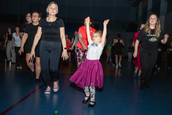 Na pierwszym planie tańcząca dziewczynka w różowej spódniczce i białej bluzce
