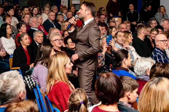 mężczyzna z mikrofonem przechadza się wśród siedzącej publiczności