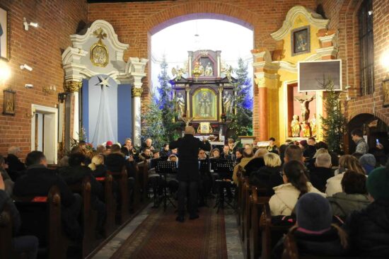 muzycy orkiestry dętej grają w kościele, publiczność siedzi w ławkach