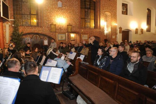muzycy orkiestry dętej grają w kościele oraz publiczność siedzi w ławkach