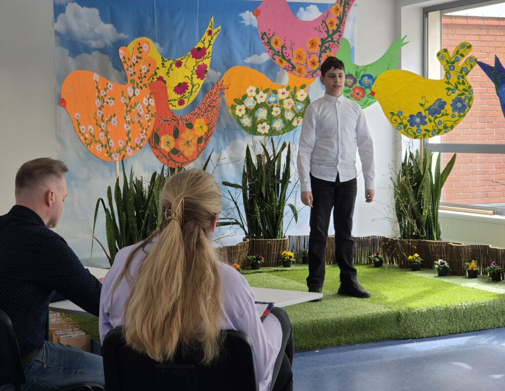 Eliminacje Gminne -chłopiec w białej koszuli stoi na scenie, na tle kolorowej scenografii