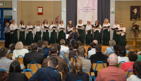 Na pierwszym planie publiczność, w tle Żeński Chór Canzona w białych bluzkach i zielonych spódnicach. Przed nimi stoi dyrygent Elżbieta Wtorkowska