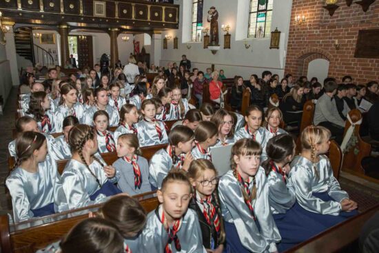 iedzące w ławkach kościelnych  chórzystki  w błękitno-niebieskich strojach z Chóru Dziewczęcego Canzona