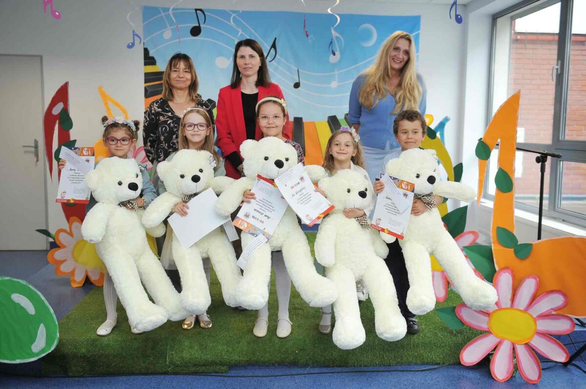 Na tle kolorowej scenografii do zdjęcia pozują laureaci i jury. Dzieci w rękach trzymają ogromne białe misie