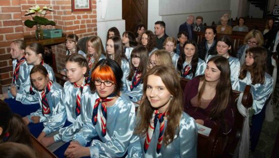 Siedzące w ławkach chórzystki  w błękitno-niebieskich strojach z Chóru Dziewczęcego Canzona