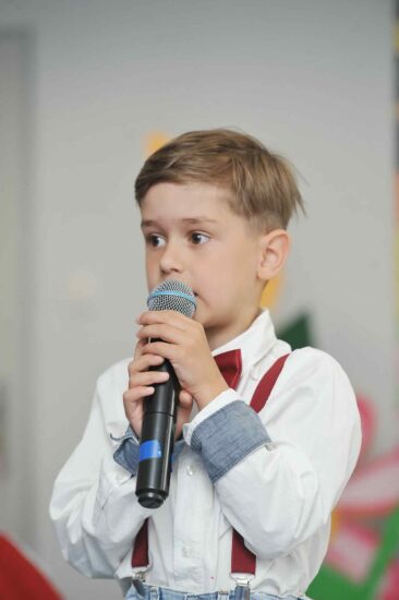 Chłopiec w białej koszuli z mikrofonem w ręku